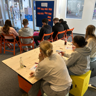 Einige Schülerinnen und Schüler sitzen in einem Raum. Sie hören gespannt zu.